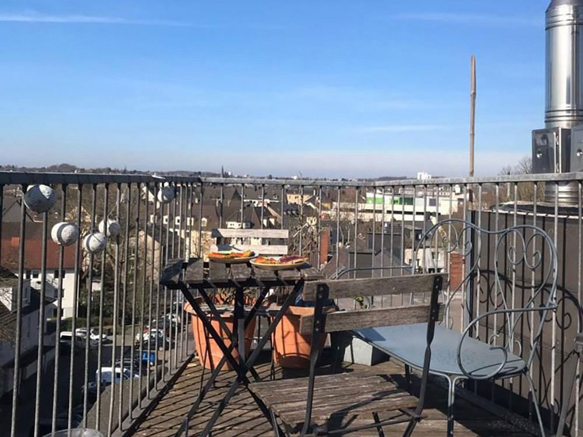 Dachterrasse mit Blick über Witten (Foto: Privat) Auf einer kleinen Dachterrasse stehen zwei Holzklappstühle, eine Bank und ein Tisch. Die Terrasse ist von einem Metallgeländer umgeben. Die Hälfte des Fotos zeigt strahlendblauen Himmel.